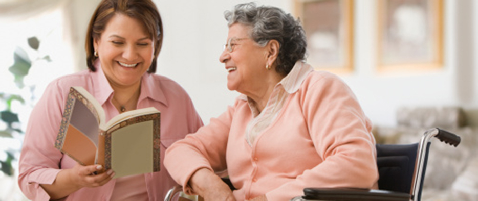 A Woman Smiling and Reading to an Elderly Woman