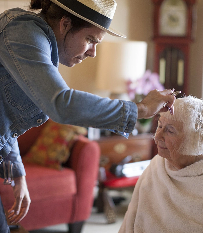 Hairdresser cuts senior woman's hair in her living room