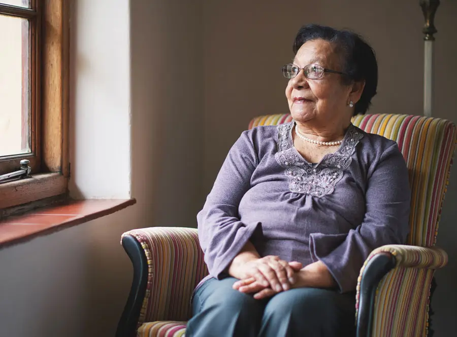 Senior woman sitting in chair looks out the window