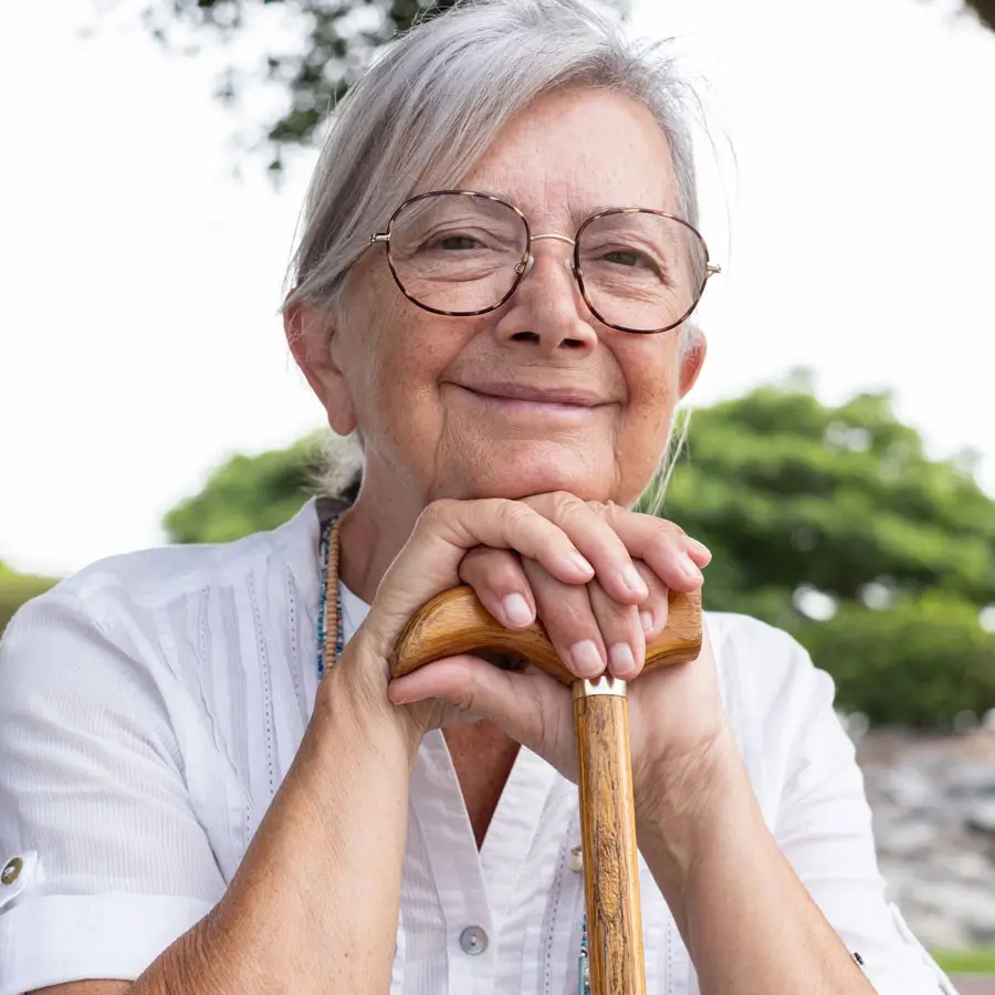 Closeup of senior woman resting hands and chin on her cane cane as she sits outside