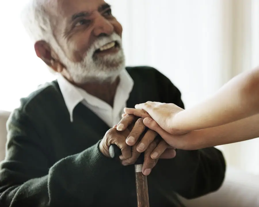 Senior man smiling as his grandchild places hands over his